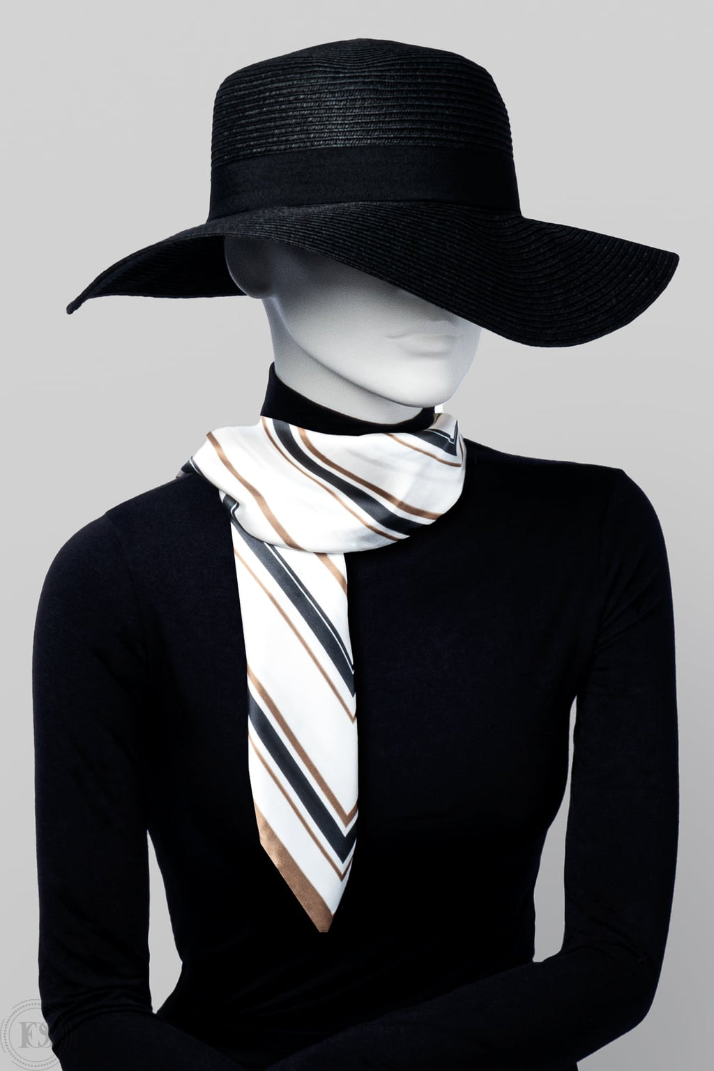 Mannequin i svart hatt och polotröja bär en elegant scarf med diagonala ränder i vitt, svart, beige och brunt, knuten löst runt halsen.
