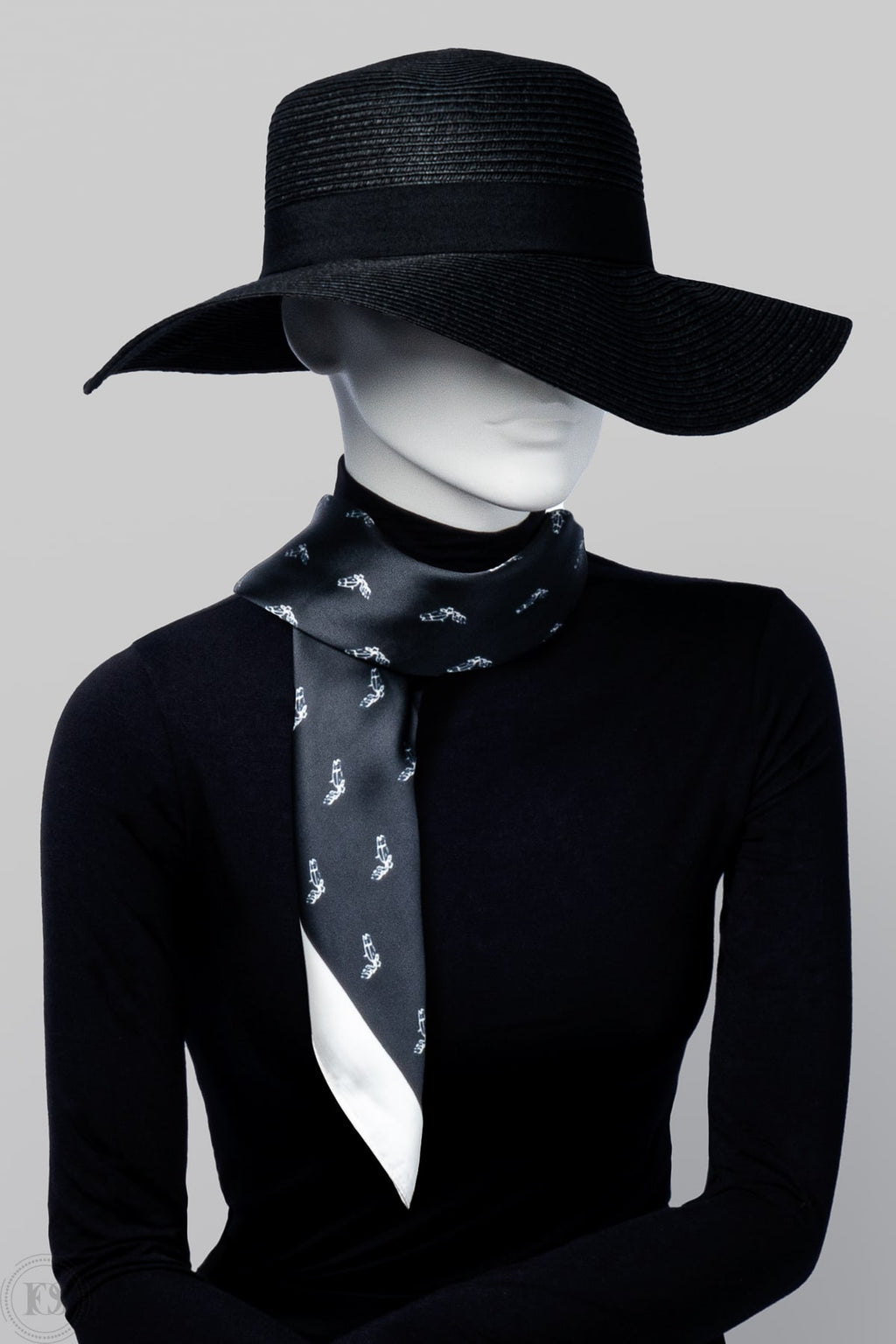 Skyltdock bär nätt scarf i silkesliknande material virat runt halsen. Svart bas med vit kant och små vita detaljmöster.