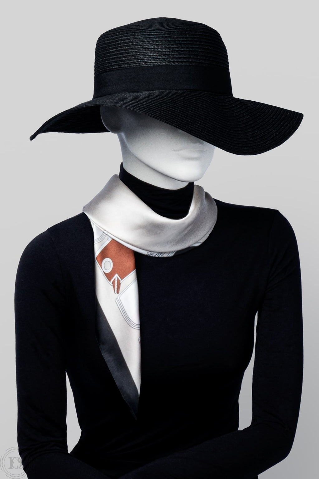 Elegant scarf i silkesliknande material i vitt, beige och terrakottafärger, stylad runt halsen på en mannequin med svart hatt och mörk topp.