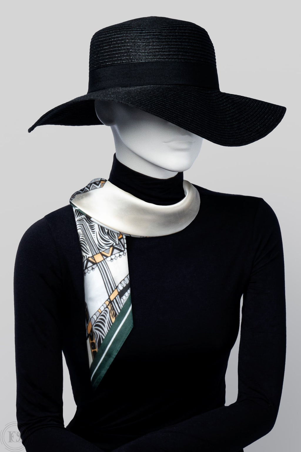 Mannequin i svart hatt och polotröja bär en elegant scarf i vit, svart, gul och gröna färger, knuten löst runt halsen.