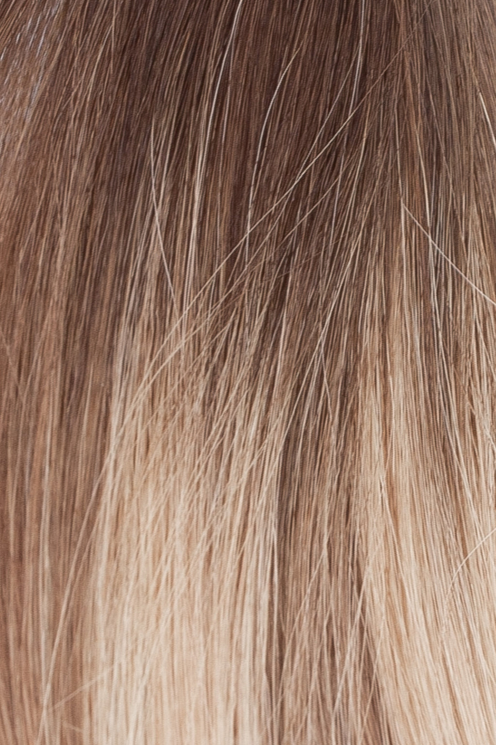 Närbild på ett färgprov av ombre-hårförlängningar i brun och blond nyans för att visa övergången och texturen.
