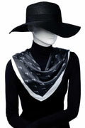 Mannequin bär svart scarf med vit kant och subtilt mönster. En stilren och tidlös accessoar i silkesliknande material.