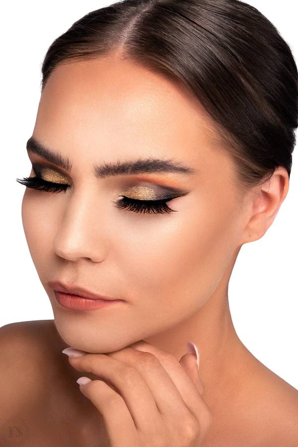 Närbild på kvinna med elegant makeup i guld- och kopparnyanser, bärandes fylliga och dramatiska lösögonfransar som framhäver ögonen.